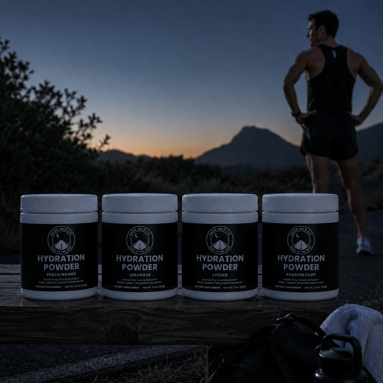 Dark Mile Co. Hydration Powder tubs lined up on a wooden bench before sunrise, with a runner overlooking a dark mountain road in the background.
