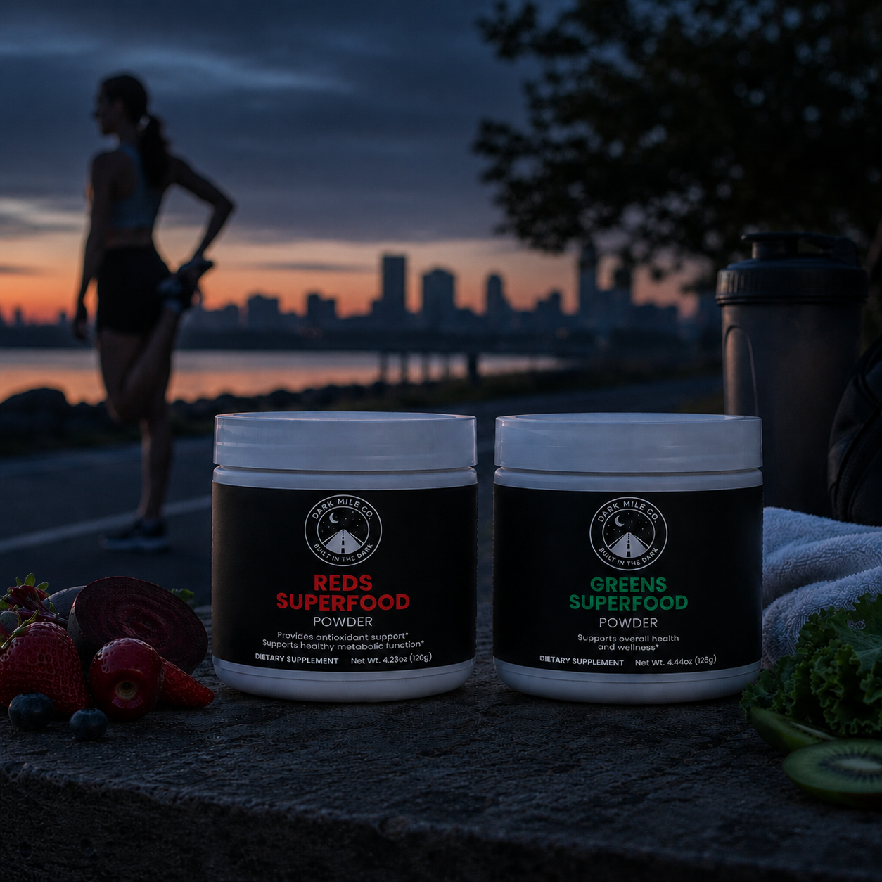 Dark Mile Co. Reds and Greens Superfood powders on a stone surface with fruit, greens, a shaker bottle, and a runner stretching by a city waterfront just before sunrise.