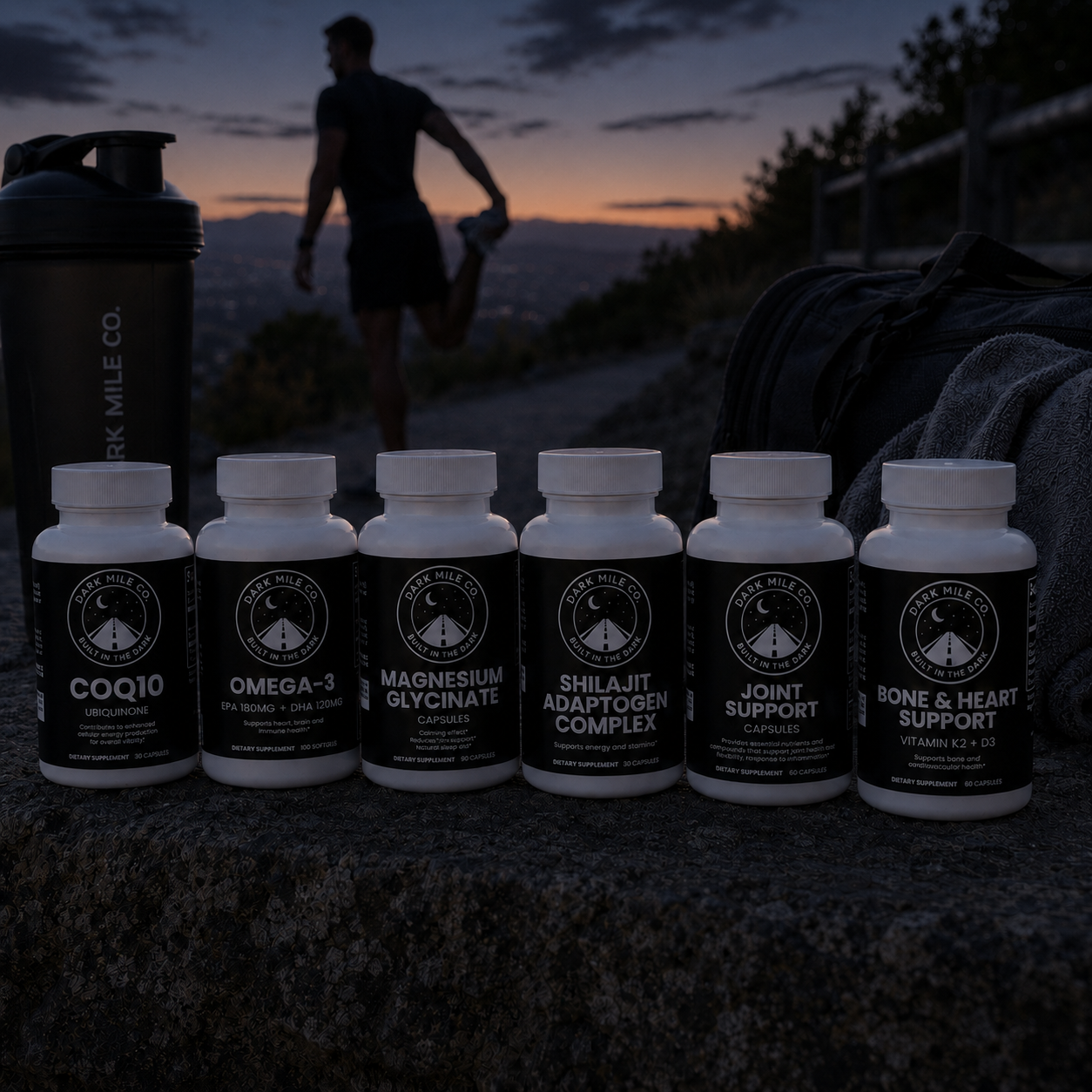 Dark Mile Co. supplement bottles lined up on a stone ledge at early dawn, with a runner stretching in the dim background beside a shaker bottle and gym bag.